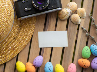 Wooden background with straw hat, photo camera, shells, colorful eggs and willow twigs. Easter card...