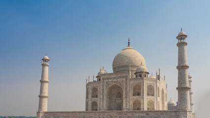 Majestic white marble Taj Mahal against the blue sky. A beautiful symmetrical mausoleum with arches, domes, spires, minarets. India. Agra