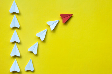 Red paper airplane origami leaving with other white airplanes on yellow background with...