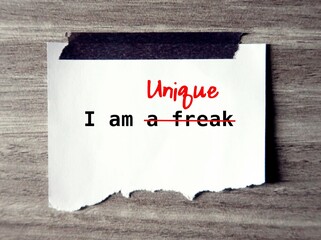 Torn paper stick on wall with message written I AM A FREAK , changed to I AM UNIQUE, means to overcome negative thoughts or self talk, accept and treat yourself with love and respect
