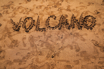 Text VOLCANO on volcanic sand. Texture, wave pattern of ocean sand on the beach. Texture of beach...