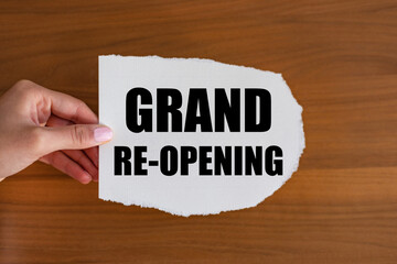 Grand re-opening. Woman hand holds a piece of paper with a note, grand re-opening. Open again,...