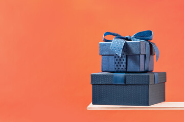 Two Luxury gift boxes with a blue bow on coral background. Side view on shelf. Fathers day or...