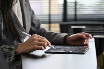 Shot of female manager sitting at black wooden office desk and using digital tablet.