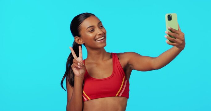 Fitness, woman and peace sign in studio for selfie, profile picture or workout vlog against a blue background. Happy, fit and sporty female smiling for photo, social media or online post on mockup
