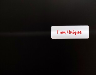 White card on black copy space background with text written I AM UNIQUE, positive affirmation which...