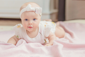 A little cute healthy girl up to a year old in a white bodysuit made of natural fabric lies on a...