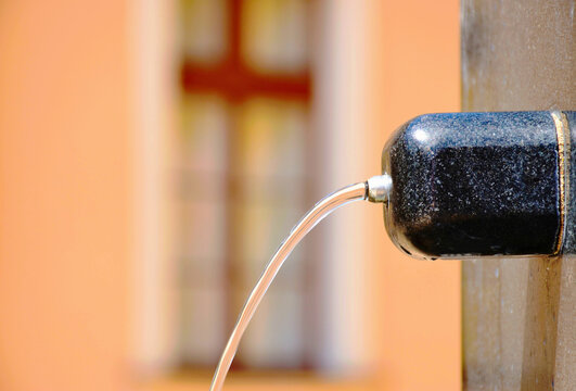 black marble water fountain spout in public park. steel water pipe and clear water stream. blurred old building facade background. blurred stucco elevation brown windows. travel and tourism concept