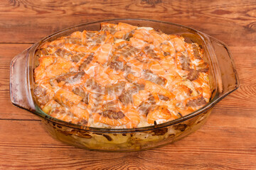 Baked vegetable casserole with salmon slices in glass baking dish