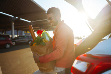 Man with a cart in the parking lot with paper bags of Hungarian products. Young man with a bag near the car. The concept of a zor lifestyle, consumerism, sale, shopping.