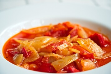 Close up of a typical hungarian homemade lecso (in hungarian: lecsó) from tomatoes, peppers and onions on white plate.           