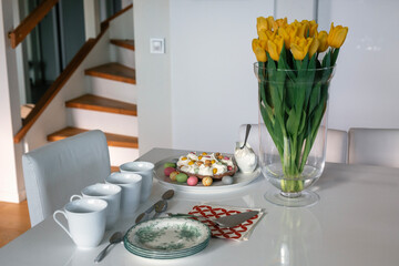 tea party for four with a cake decorated with Easter eggs, organized as a buffet and decorated with yellow tulips