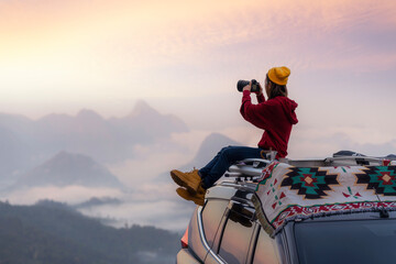 Traveller woman sit on the roof top tarp and car and drink a coffee with morning sunrise and fog on...