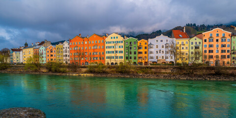 Innsbruck city skyline on a April day with vibrant colorful houses, the snowy Alps mountains, foggy cloudscape, the green Inn River in historic landmark town of Tyrol in western Austria