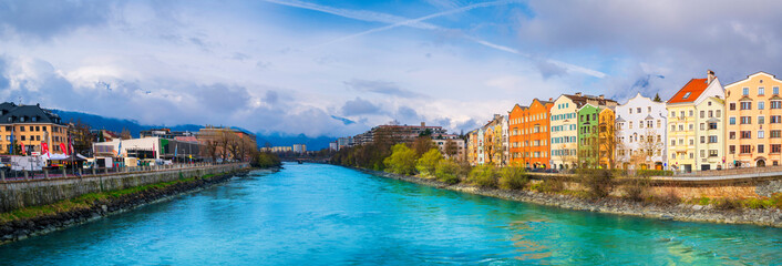 Fototapeta na wymiar Innsbruck city skyline on a April day with vibrant colorful houses, the snowy Alps mountains, foggy cloudscape, the green Inn River in historic landmark town of Tyrol in western Austria
