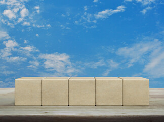 Five wood block cubes on wooden table over blue sky with white clouds