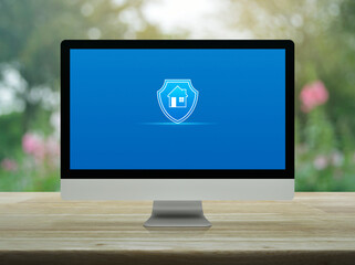 Home with shield flat icon on modern computer monitor screen on wooden table over blur pink flower...
