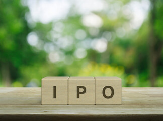 IPO letter on wood block cubes on wooden table over blur green tree in park, Initial public...