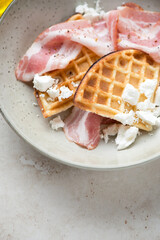 Close-up of belgian waffles with bacon and feta cheese, vertical shot on a beige stone background, selective focus