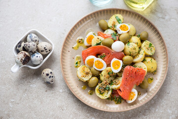 Plate with potato, smoked trout fillet and boiled quail eggs salad, high angle view on a beige stone background, horizontal shot
