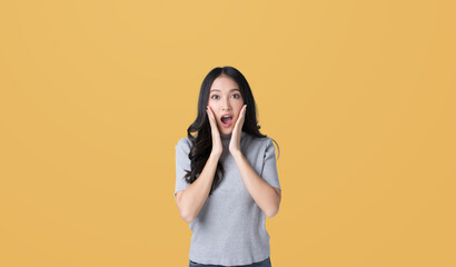 Young Asian doing a shocked surprise gesture with her hands on her face isolated yellow color...