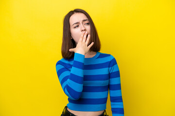 Young Ukrainian woman isolated on yellow background yawning and covering wide open mouth with hand
