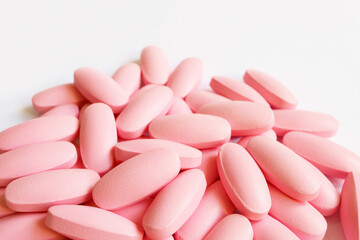 Heap of pastel pink supplement pills on white background with copy space