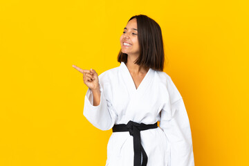 Young woman doing karate isolated on yellow background pointing finger to the side