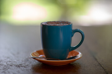 A blue cup of cappuccino on the orange plate with a spoon and blurred background