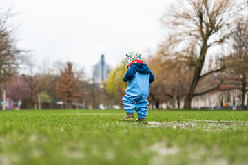 A little child playing in a puddle in a park during rainy weather