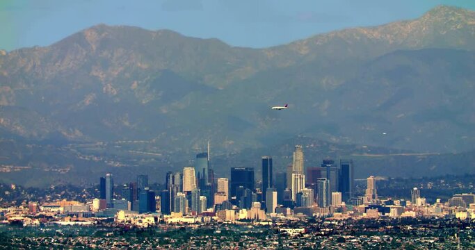 Airplane flies over Los Angeles Downtown financial and business towers skyscrapers skyline with mountains in the background, California. 