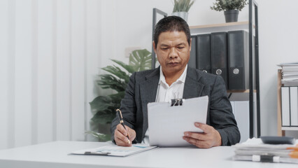 Fototapeta premium Reading paper charts, Elderly Old Senior Asian male businessman wearing formal suit ,confident professional bookkeeper doing bookkeeping, lawyer, stock market trader or broker.