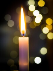 Vertical closeup of a beautiful flaming candle with bokeh lights in the background