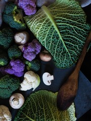 Vertical top view shot of numerous types of green vegetables with a wooden spoon beside them