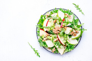 Waldorf salad with red and green apple, green celery, lettuce, arugula and walnuts on plate, white table background, top view