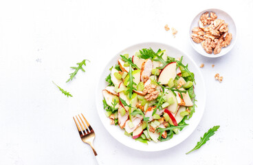 Waldorf salad with red and green apple, celery, lettuce, chicken fillet, arugula and walnuts on plate, white table background, top view