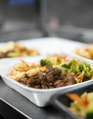 Vertical shot of a lunchbox with roasted beef, salad, and shrimp on the table