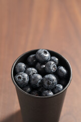 Blueberries in black paper cup on walnut table