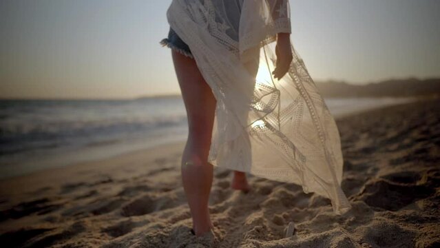 Woman in a white beach cover-up walking along the beach at sunset in Mexico.