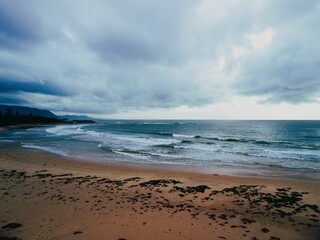 Scenic shot of foamy ocean waves crashing on a sandy coast surrounded by a mountain range