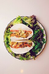 Vertical top view shot of two tacos served on vegetables on a white glass plate