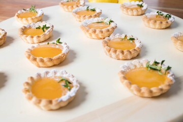 Closeup shot of numerous small lemon tarts on a wooden plate