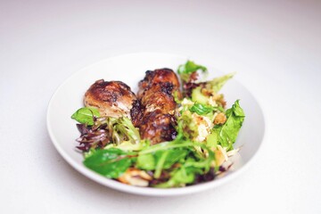 High angle closeup shot of a rustic chicken meal served with a salad in a white bowl