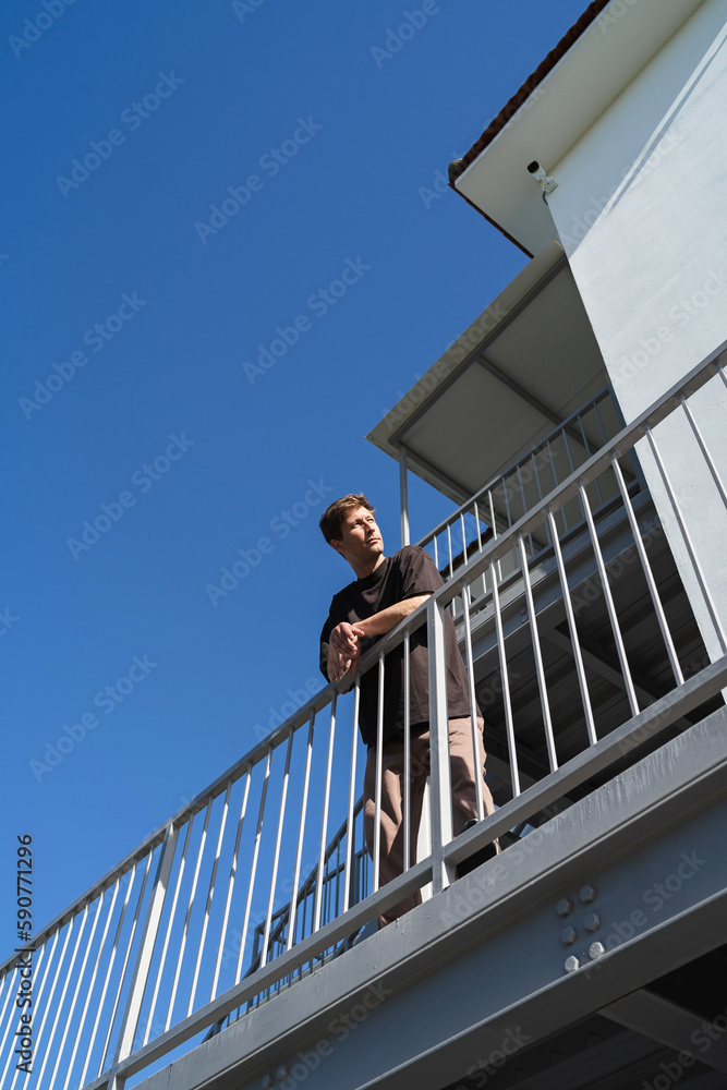 Wall mural Low angle of young man standing beside apartment complex on his neighborhood