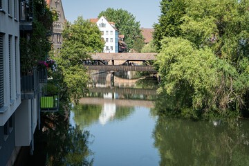 Naklejka premium Bridge, trees, and buildings reflected on the Pegnitz river on a sunny day