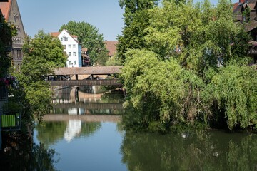 Fototapeta na wymiar Bridge, trees, and buildings reflected on the Pegnitz river on a sunny day