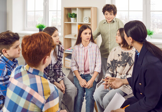 School children discussing something in class. Group of elementary students together with their teacher sitting in a circle in the classroom and talking about the book that they have read today