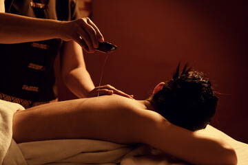 Masseur pouring aroma oil on back woman customer in cosmetology spa centre.