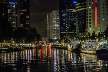 Ships on the river in Rotterdam at night with the reflection of surrounding buildings on its surface