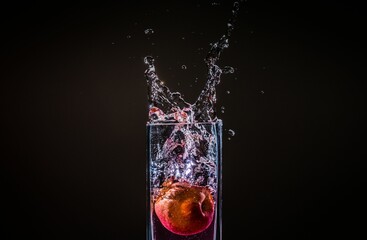 Water splashing out from a glass with an apple in it in isolated on a black background